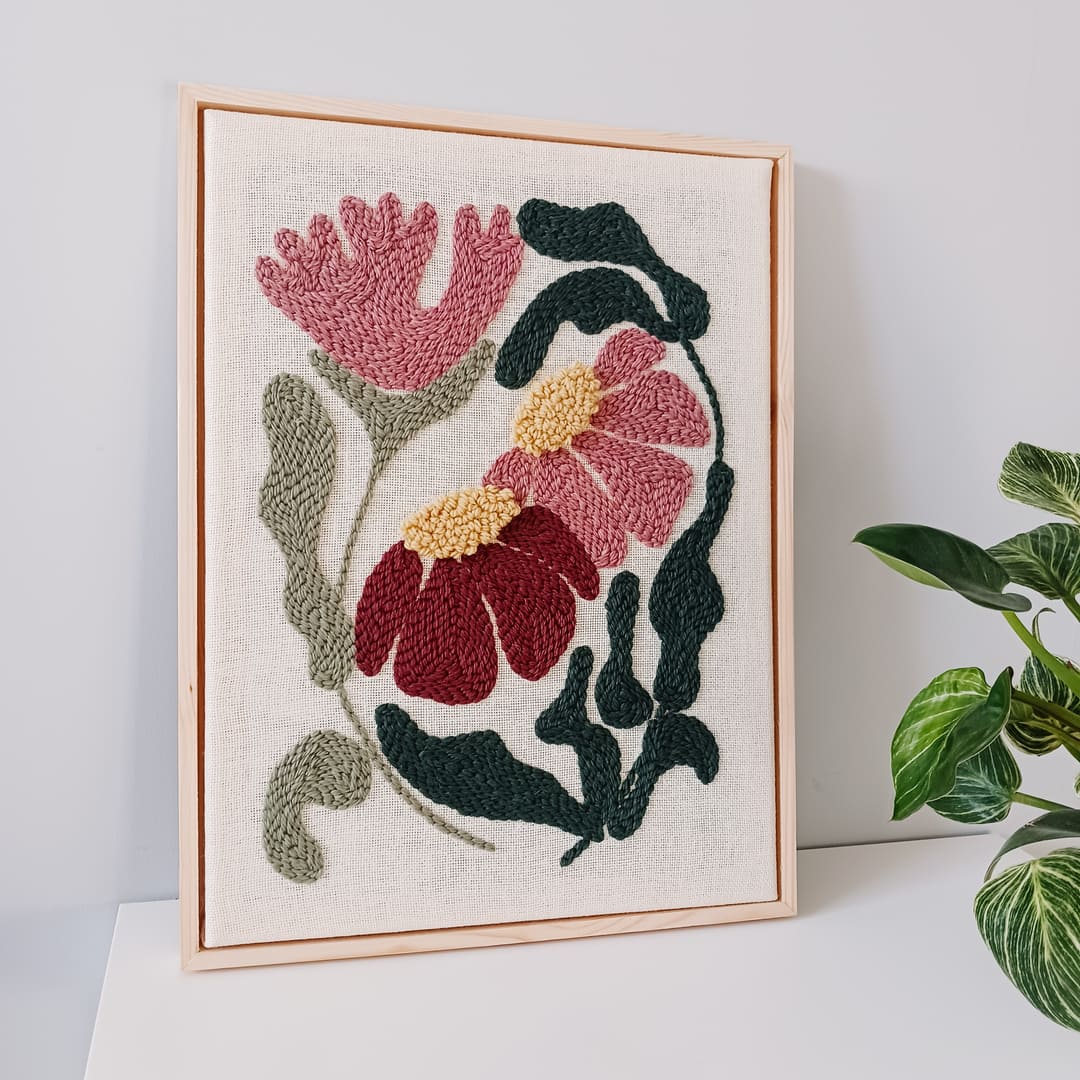 Ręcznie wykonany obraz techniką punch needle w odcieniach różu i zieleni oprawiony w wąską drewnianą ramkę. Dekoracja ścienna o kwiatowym wzorze, idealna do nowoczesnych i przytulnych wnętrz.