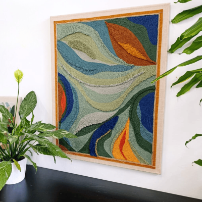 Ręcznie wykonany obraz techniką punch needle w odcieniach zieleni, niebieskiego, pomarańczu i żółci. Dekoracja ścienna o abstrakcyjnym, organicznym wzorze, idealna do nowoczesnych i przytulnych wnętrz.
