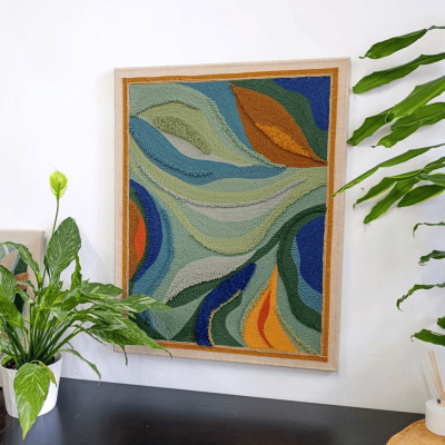 Ręcznie wykonany obraz techniką punch needle w odcieniach zieleni, niebieskiego, pomarańczu i żółci. Dekoracja ścienna o abstrakcyjnym, organicznym wzorze, idealna do nowoczesnych i przytulnych wnętrz.