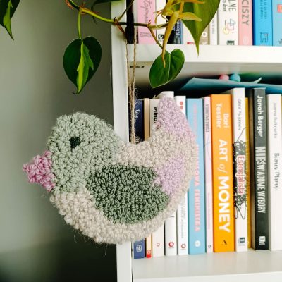 Zawieszka ścienna z wełnianych pętelek w kształcie ptaszka.