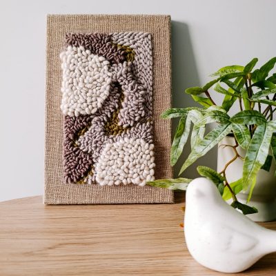 Obrazek wełniany z abstrakcyjnym motywem w kolorach ziemi.